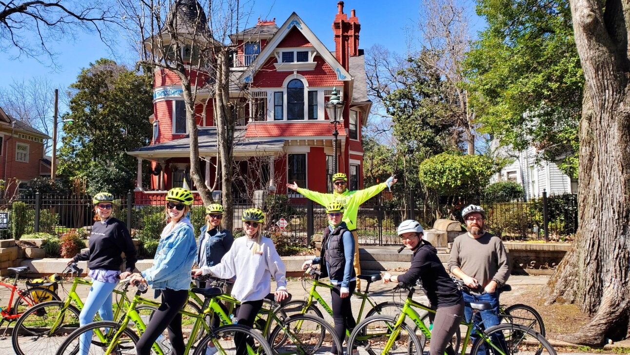 A group of cyclists pose for a photo in front of historic houses in Atlanta, Georgia