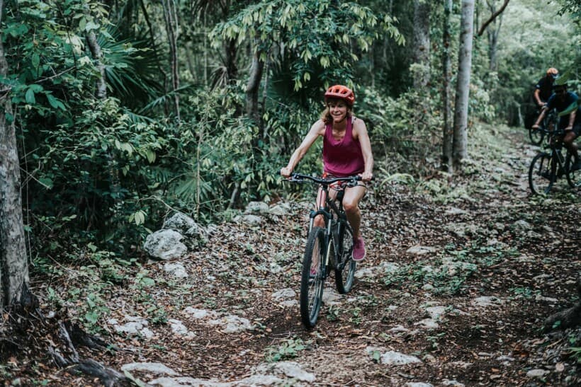 A woman smiles while riding a mountain bike through the forest