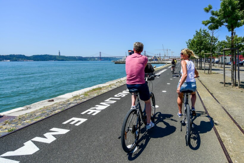 Cyclists ride along the sea in Lisbon, Portugal with the 25 April bridge in the background