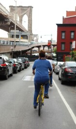 A cyclist rides in lower Manhatten with a view of the Brooklyn Bridge