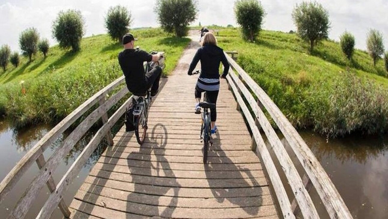 2 people bike across a bridge outside Amsterdam