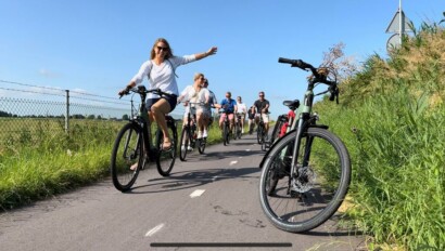 A group of cyclists ride along a bike path amidst tall grass