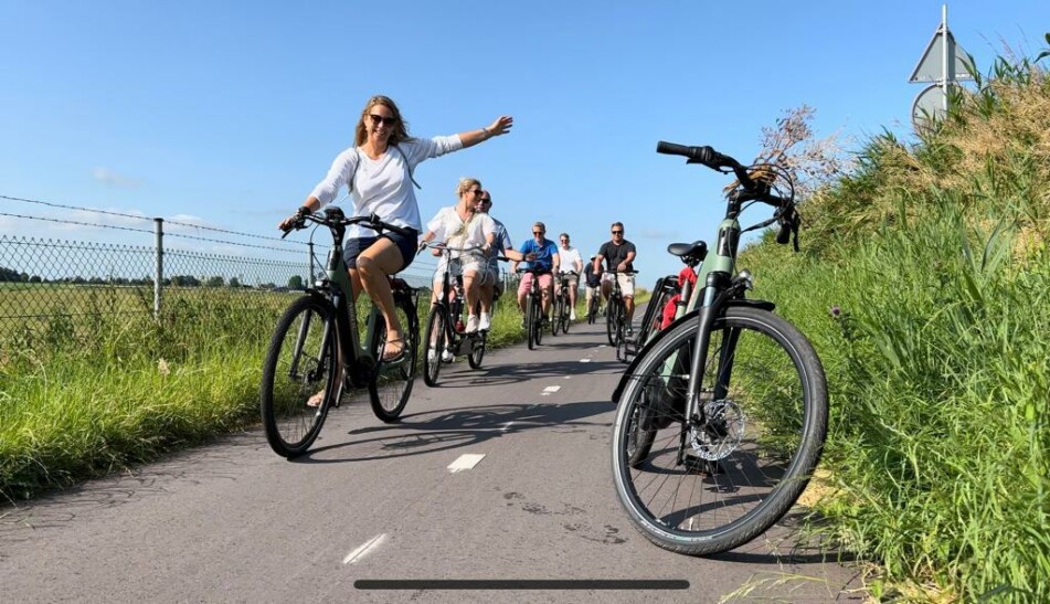 A group of cyclists ride along a bike path amidst tall grass